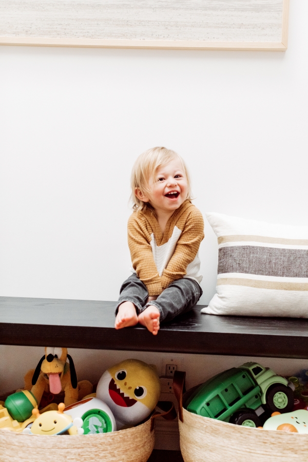 toddler laughing with toys organized under a bench in baskets by Kimberly Lapides of eatsleepwear