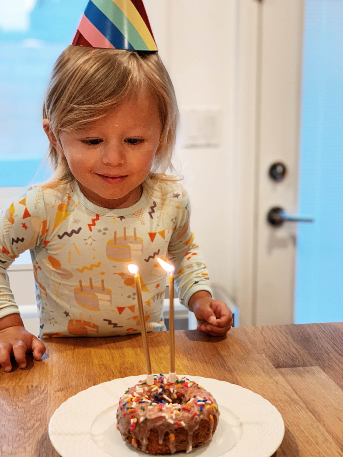 Otis blowing out birthday candle wearing rainbow party hat for Trolls Theme Birthday