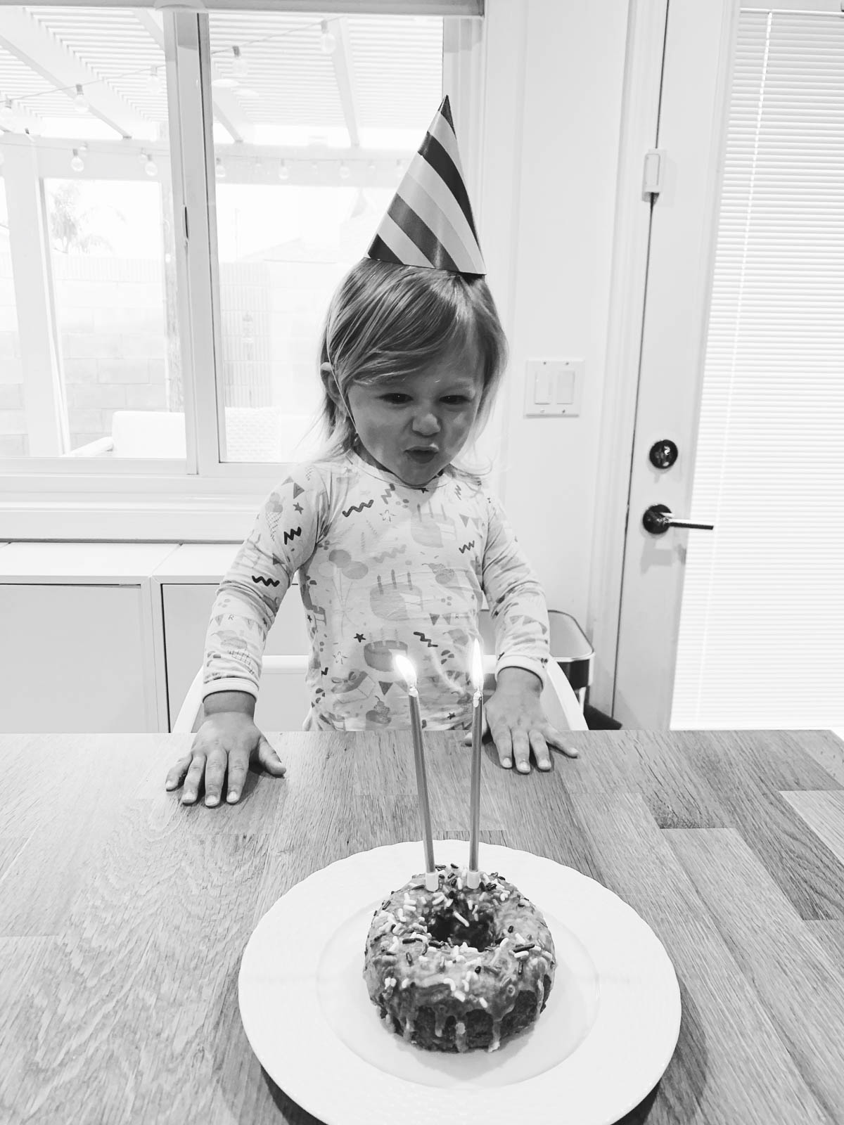 Otis blowing out birthday candle wearing rainbow party hat for Trolls Theme Birthday