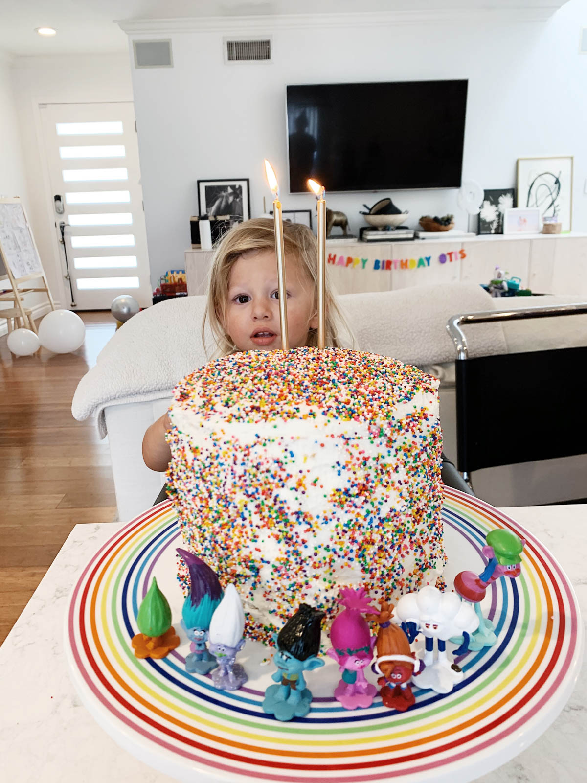 Otis eating DIY rainbow sprinkle cake with Trolls figurines for Trolls theme birthday