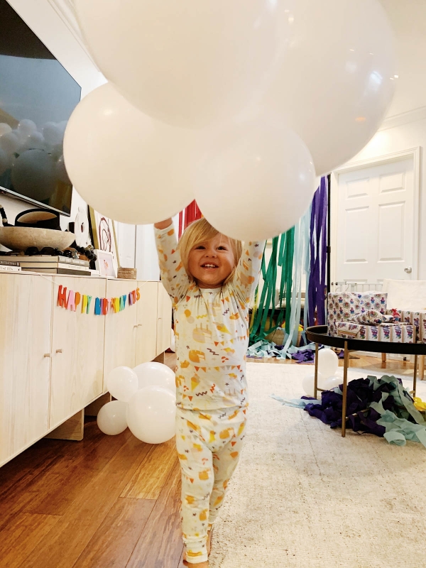 Otis playing with balloons and DIY Rainbow and cloud balloon arch with streamer backdrop for Trolls Themed Birthday