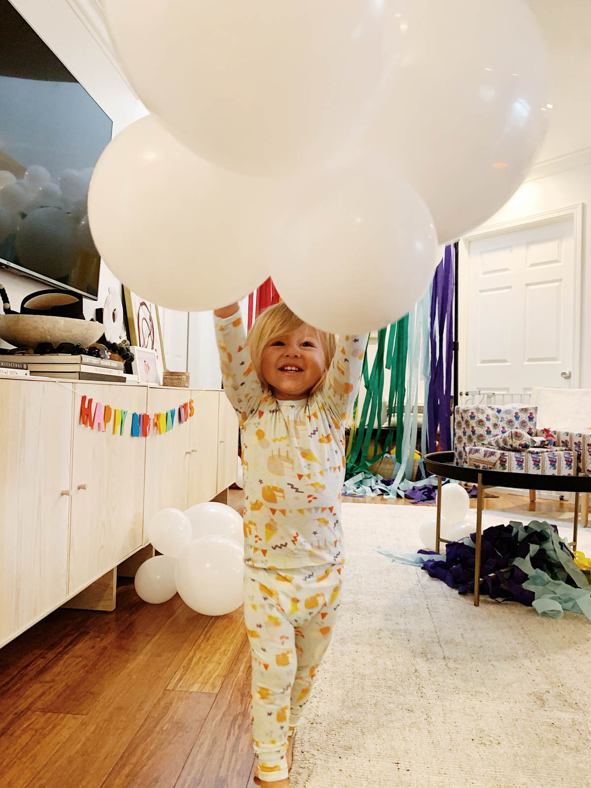 Otis playing with balloons and DIY Rainbow and cloud balloon arch with streamer backdrop for Trolls Themed Birthday