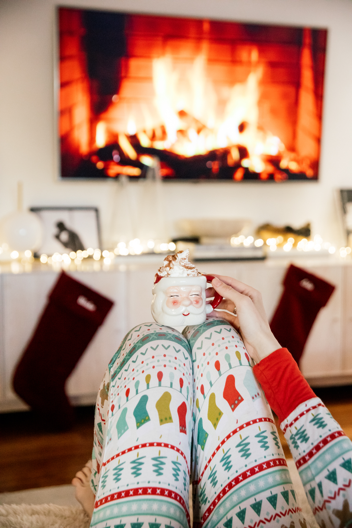 Indoor Holiday decor of twinkle lights tree, twinkle lights, clear glass Christmas tree cloche, and custom embroidered stockings and santa clause mug with hot chocolate
