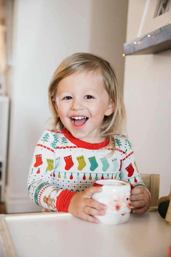 Indoor Holiday decor of toddler sitting at kids table with Santa Clause mugs in Christmas pajamas