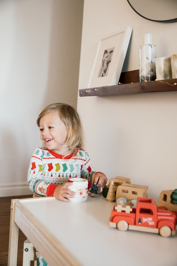 Indoor Holiday decor of toddler sitting at kids table with Santa Clause mugs in Christmas pajamas
