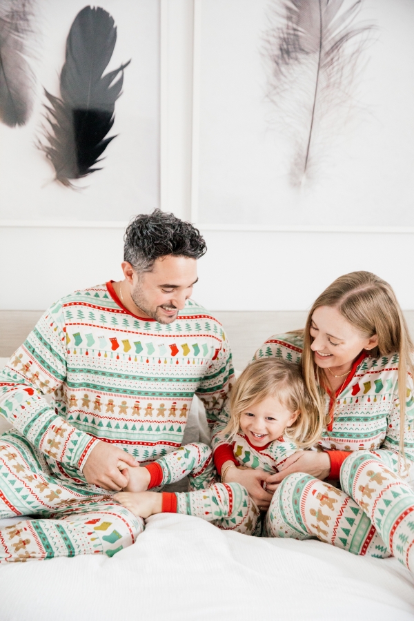 Family in matching Holiday pajamas laughing on the bed