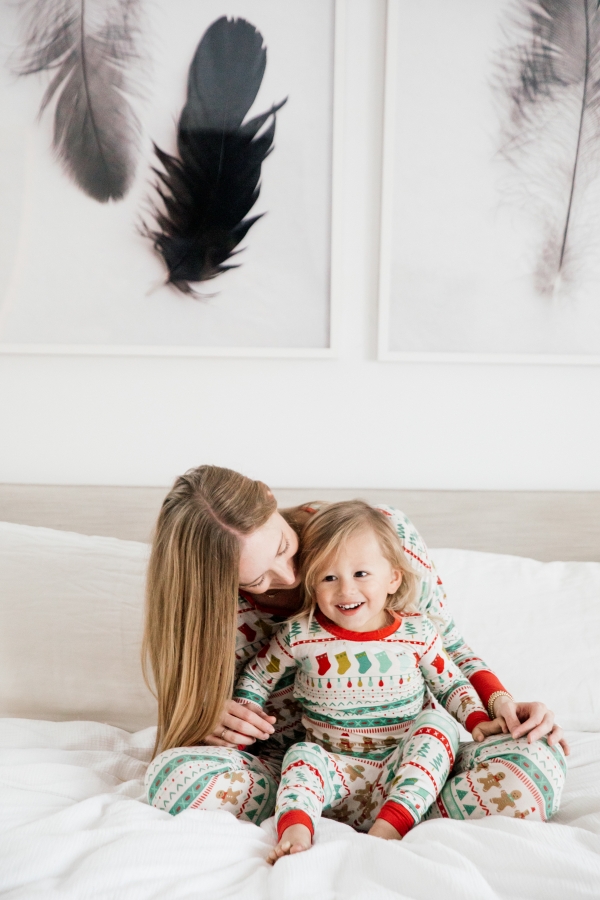 Mother and son in matching Holiday pajamas laughing on the bed